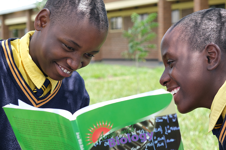 Image of two Kuwala students looking into a Buology workbook. 