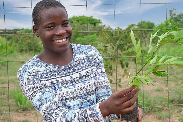 Image of Kuwala student smiling as she is holding a tree she is about to plant. 