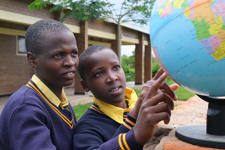 Image of Kuwala girls looking at a globe of the world pointing to Canada.