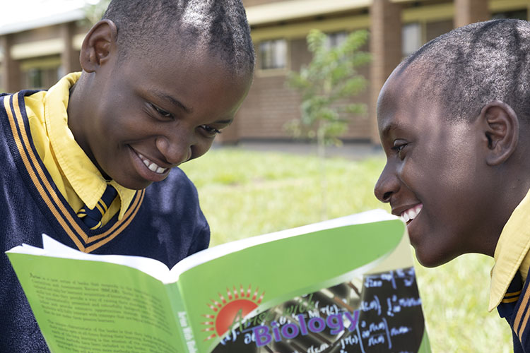 Two Kuwala students sharing a text book with smiles on the faces.