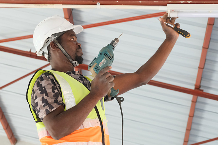 Tradesperson working with drill and screwdriver to install lighting in St. Peter's Assembly hall ceiling. 