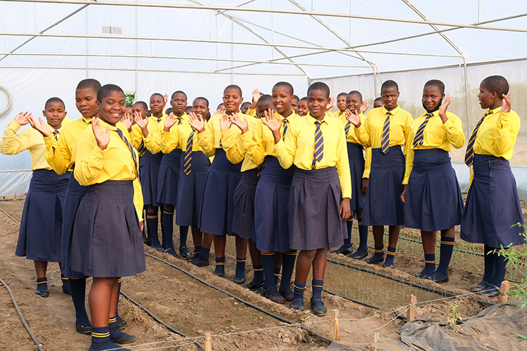 Large group of Kuwala students in the new greenhouse smiling and waving. 