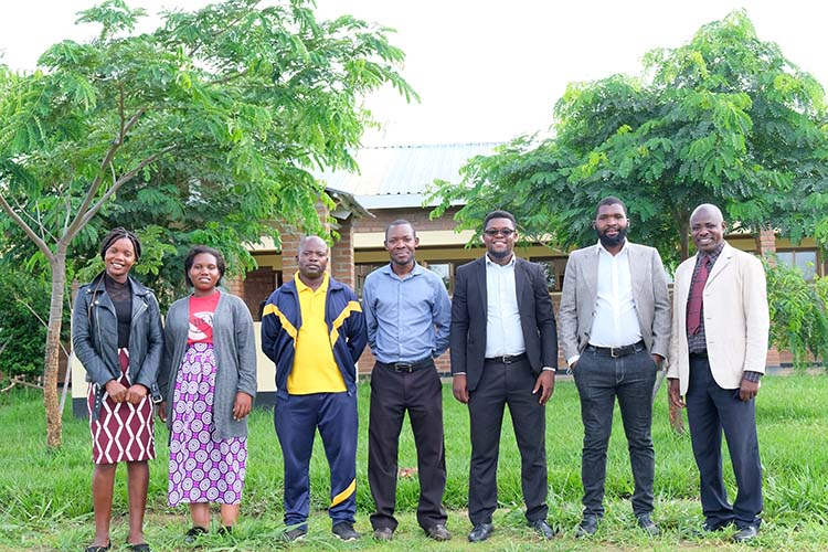 Kuwala's teaching staff in front of classroom block surrounded by lush greenery.