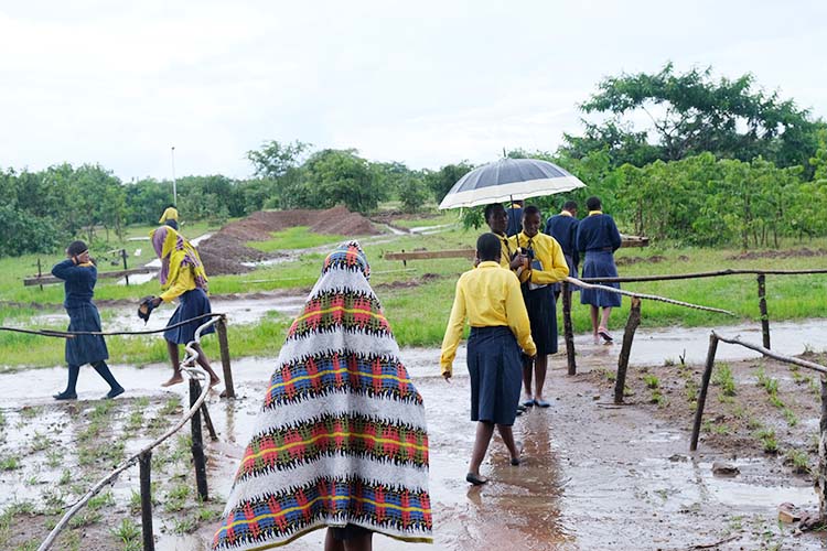 Students outside in the rain walking through muddy sidewalk.