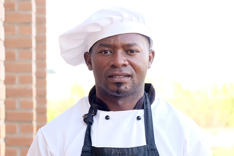 Mr. Phillius Kupeta standing outside with his chef's hat on.