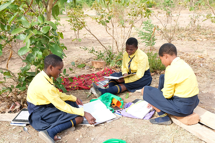 Group of Kuwala students seating on the ground with their study workbooks open.