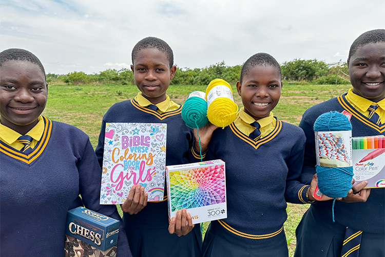 Kuwala students with balls of yarn and colouring books with the soccer field in the background.