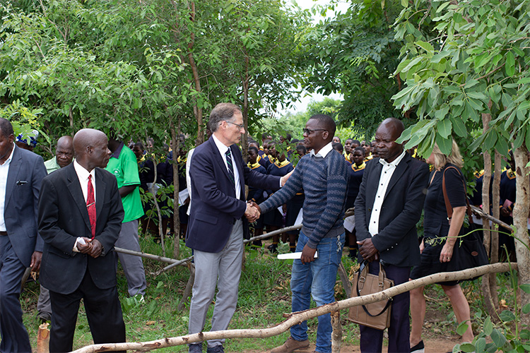 Mark Kinzel shaking hands with trees surrounding the image and the Kuwala students in the background.
