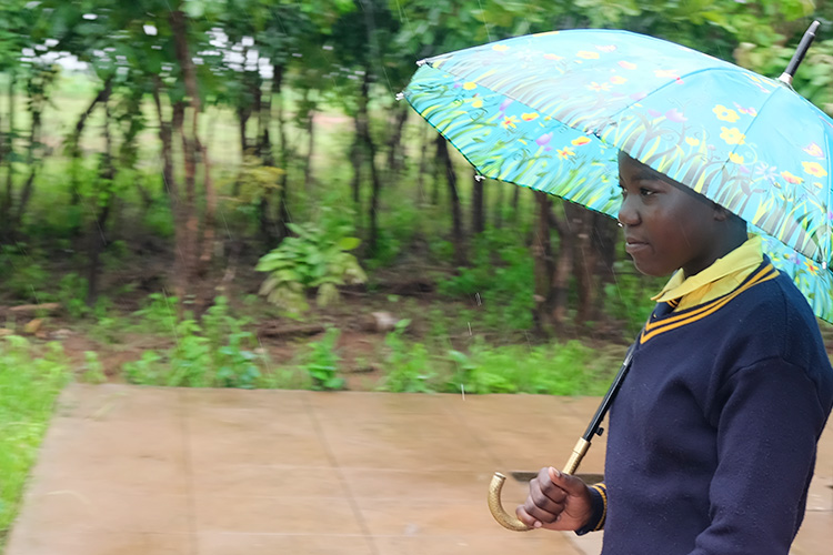 Kuwala's student Caroline with blue umbrella just outside the classroom block. 