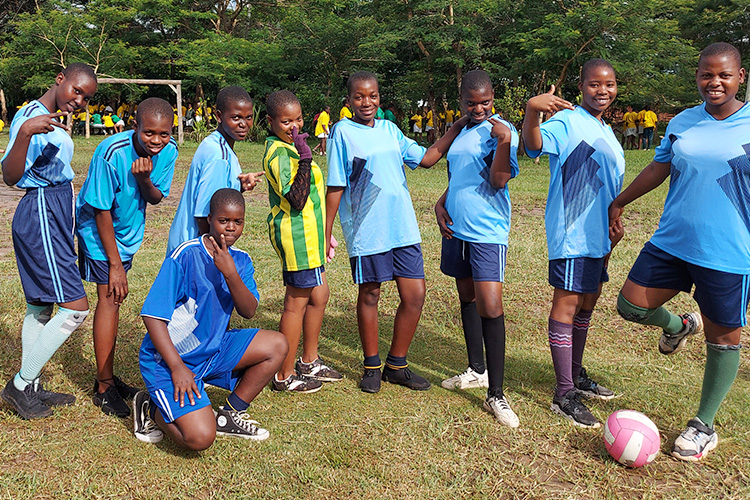 Kuwala students posing kneeling and standing by soccer ball. 