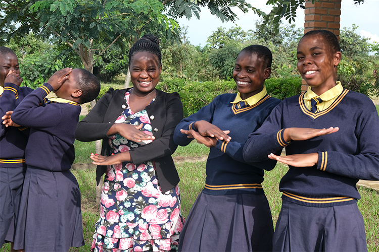 Students and teacher posing outside with trees in the background. 