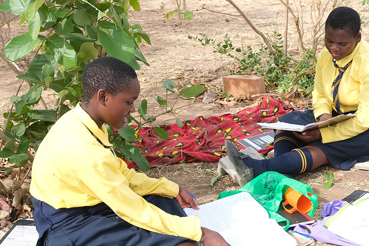 Kuwala girls sitting down outside reading.