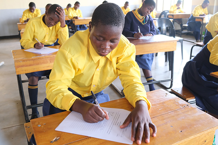 A couple of Kuwala students writing in the classroom on wooden desks.