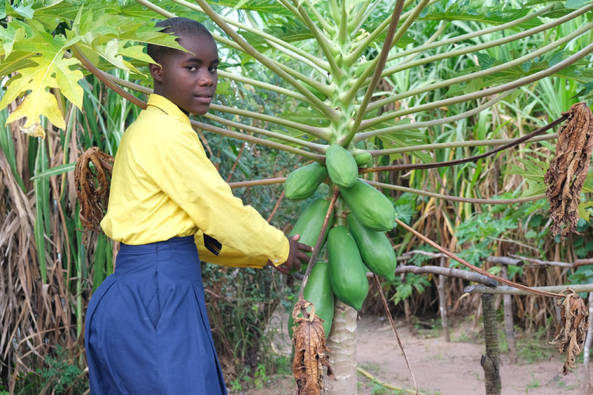 Martha a Kuwala student poses in front of a fruit tree in the orchard.