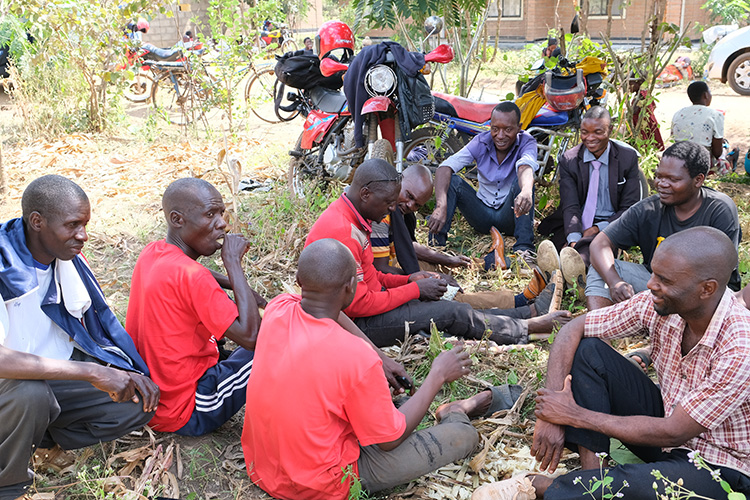 Parents of the student candidates gather outside the campus with motorbikes in the background.