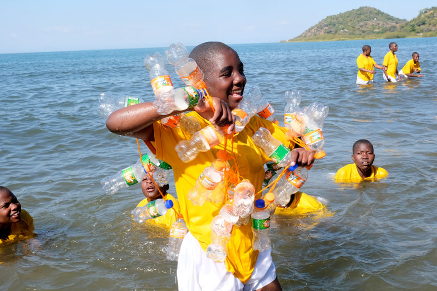 Kuwala students in the water in Lake Malawi with empty pop bottles testing out the life jacket made with the empty bottles.