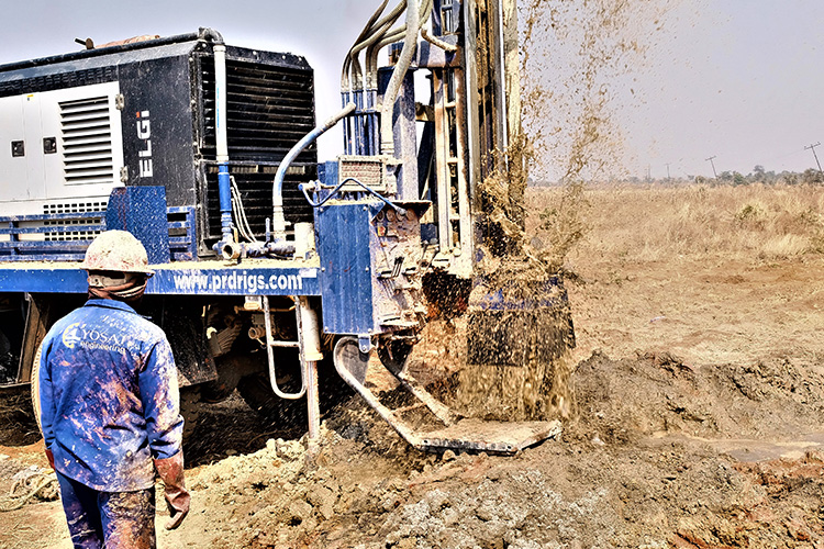 Workers observing a new borehole exploding with water as the machine bores.
 