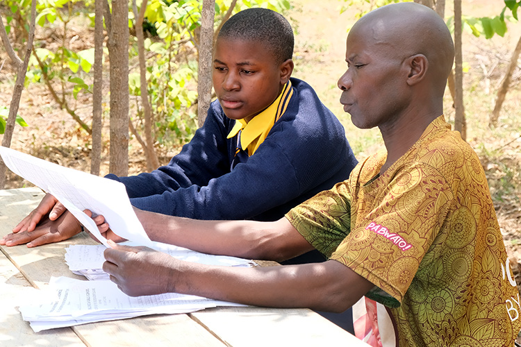 Parent and the daughter at a picnic table reviewing student's grades under an tree.