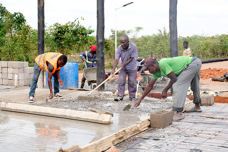 Workers leveling concrete floor in the construction of the Campus workshop.