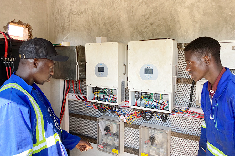 Two workers installing the solar power inverters inside the power building on Campus.