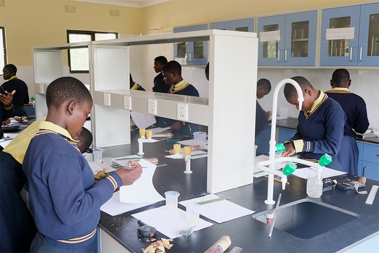 Kuwala students in uniform working in the new science lab with chemistry equipment on the counter.