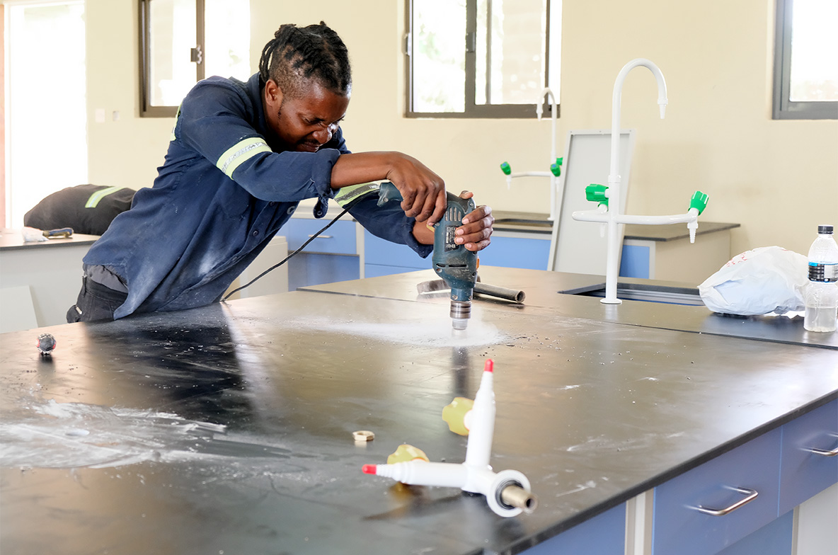 Worker drilling hole in desk top cabinet in the science lab