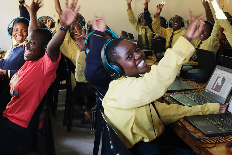 Group of students smiling in the computer lab with hands in the air. 