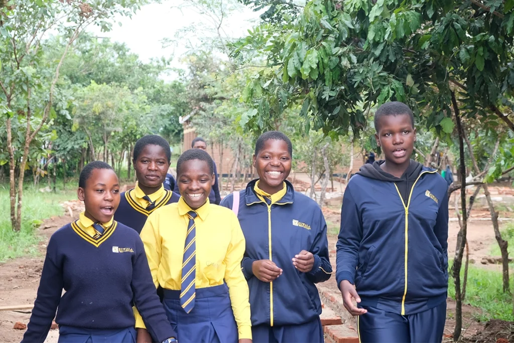 Kuwala students walking to class outside with lots of trees in background.