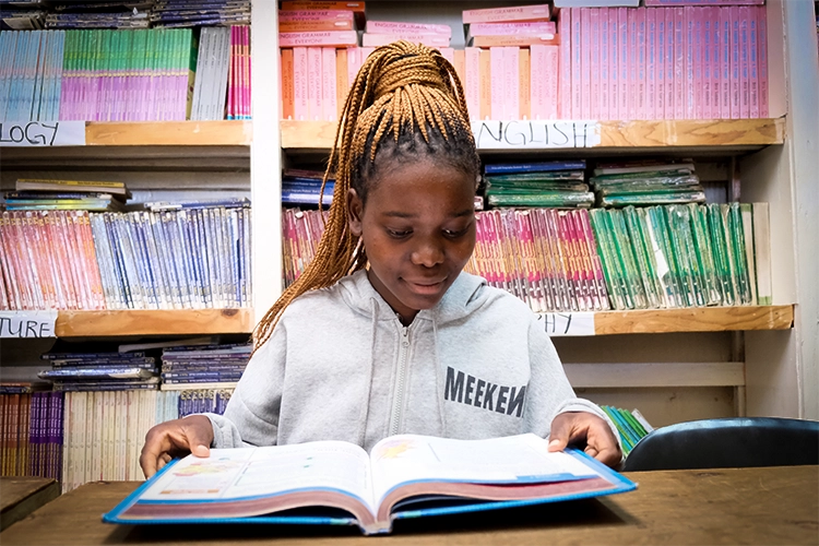 Irene studying in the Kuwala library with workbooks on a shelf behind her.