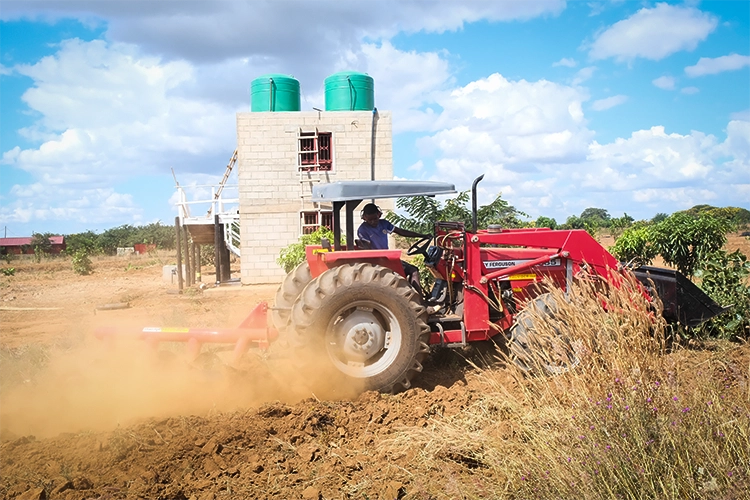Tractor working in the field with a farm implement blade on the back. The background is showing the new second water tower under construction.