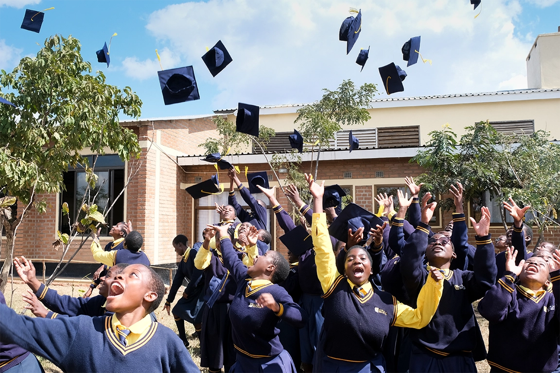 Group of Kuwala grads throwing hats outside St. Peter's Assembly Hall