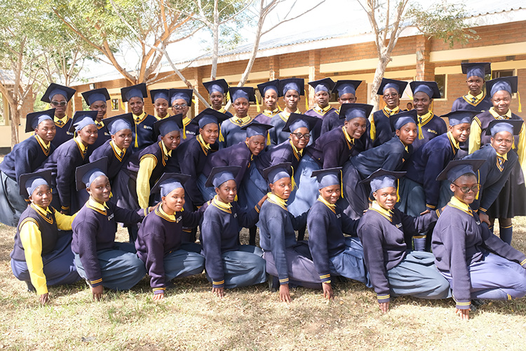 Grouping of Kuwala 2025 Grads in front of a classroom block kneeing. 