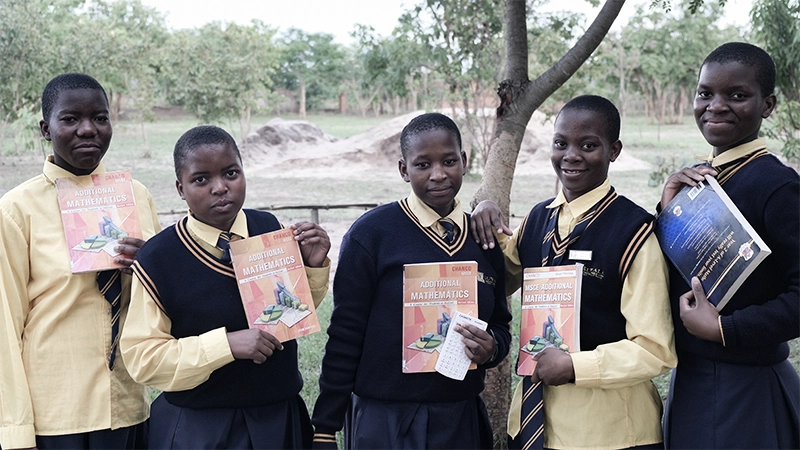 Kuwala math students holding their workbooks in a row outside with their uniforms on. 