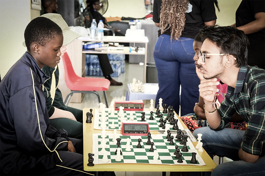 Kuwala. student playing chess seating down at the chess board with a man contemplating his next move.
