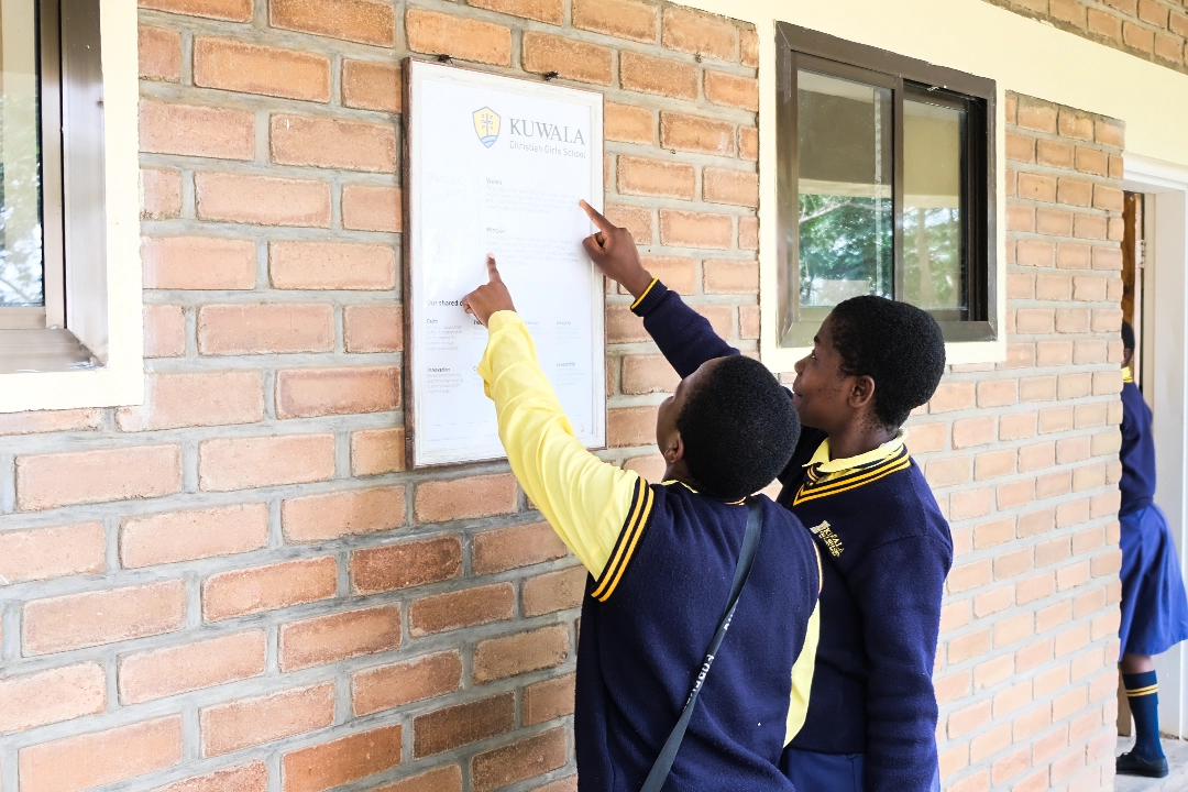 Kuwala-Mission-Statement-Poster-DSCF7215 Two Kuwala students pointing at the Mission Statement outside the classroom block.