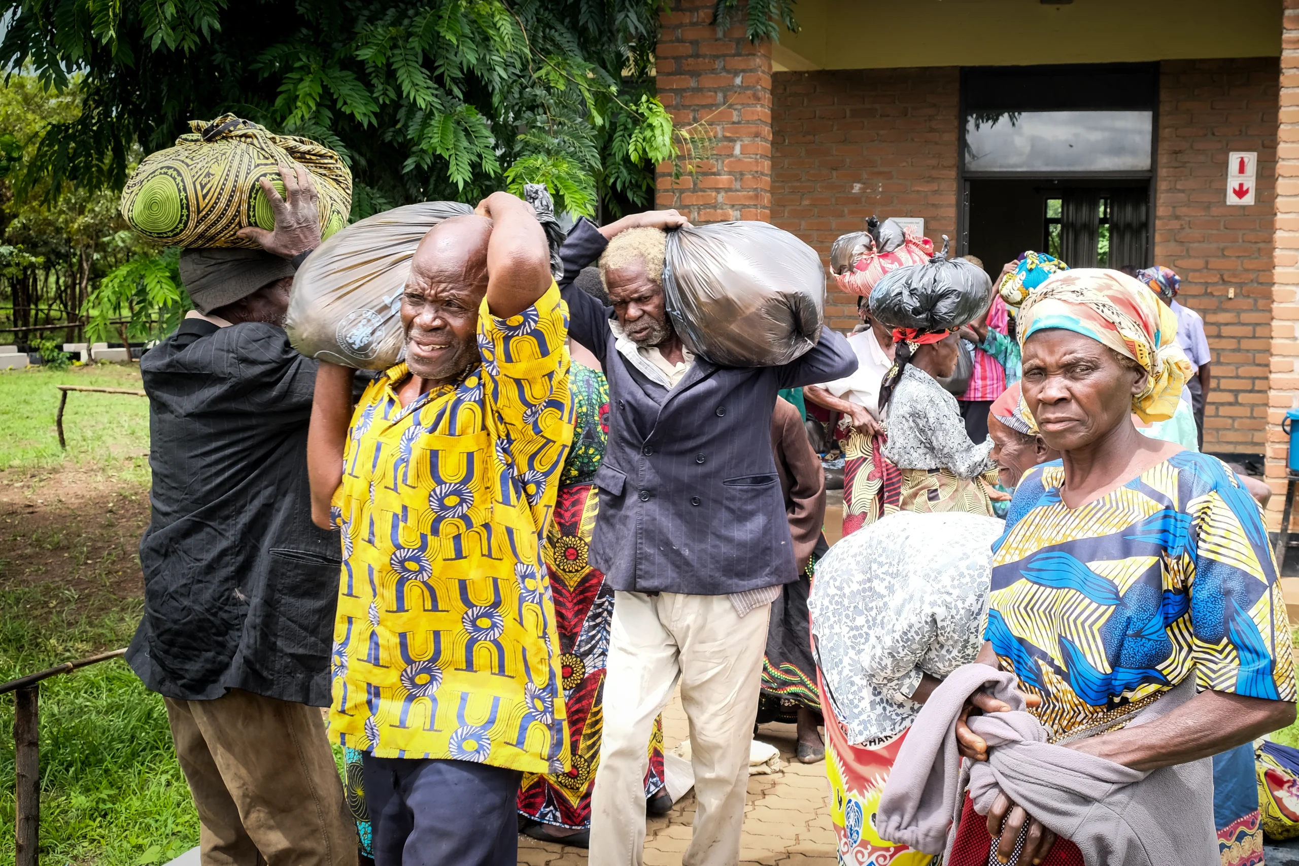 Kuwala-Villagers-Hampers-Christmas-DSCF6600 Villagers visiting Kuwala outside St. Peter's Assembly Hall with sacks of grain on mens' shoulders.