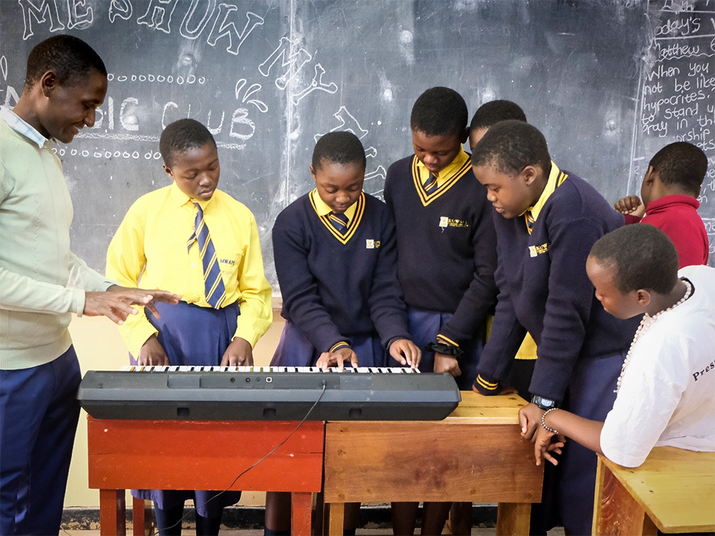 Kuwala students and male teacher gathered around a electronic music keyboard.